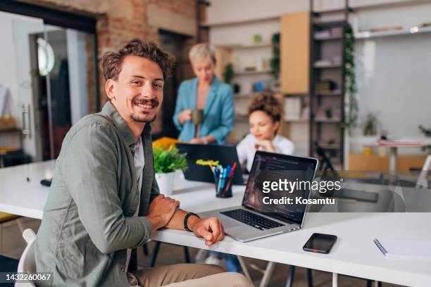 ein fröhlicher mann sitzt seinen beiden kolleginnen an einem konferenztisch gegenüber und lernt programmieren - co workers looking at computer stock-fotos und bilder