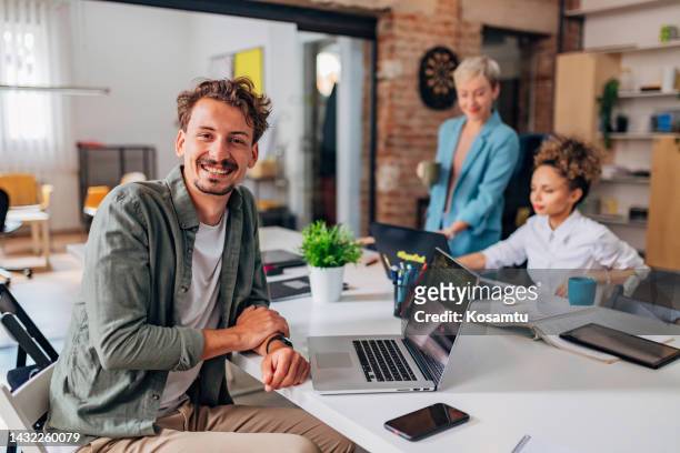 portrait of a smiling man looking directly into the camera while sitting at a desk and using a laptop to code - java stockfoto's en -beelden
