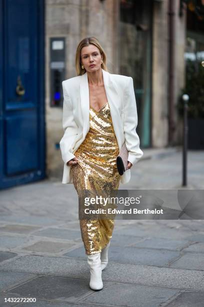 Elizabeth Sulcer wears gold and white pearls earrings, a white ribbed oversized / shoulder pads blazer jacket, a gold sequined / v-neck long dress,...