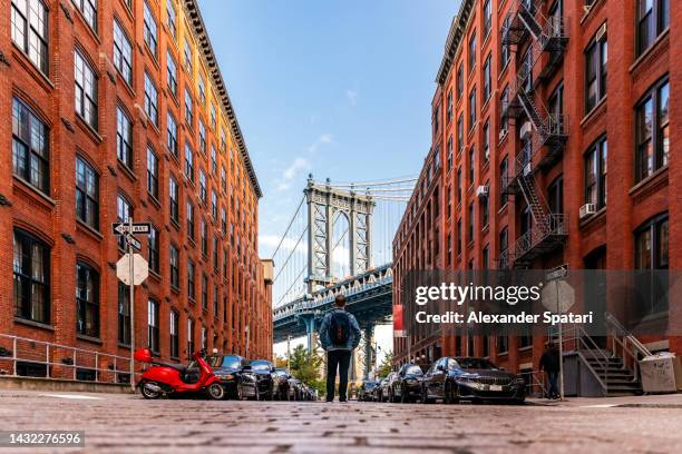 man with backpack looking at manhattan bridge from dumbo brooklyn, new york city, usa - dumbo new york fotografías e imágenes de stock