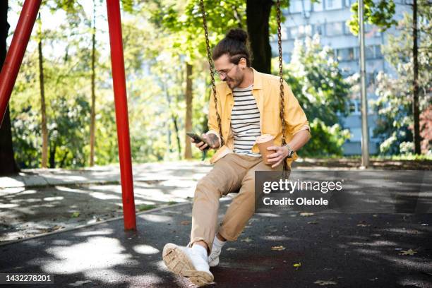junger mann schwingt, kaffee genießt und surft im netz - schaukel mann stock-fotos und bilder