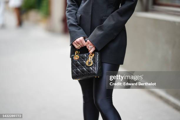 Sira Pevida wears a black shoulder-pads / blazer jacket, black nylon tights, a black shiny leather Lady D-Light handbag from Dior, outside Victoria...