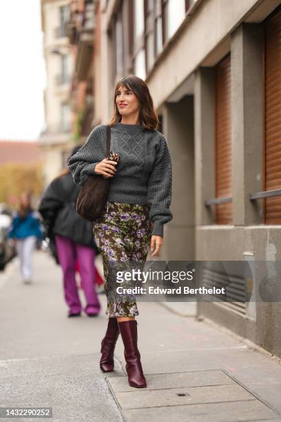 Jeanne Damas wears gold earrings, a dark gray braided wool pullover, a dark brown suede shoulder bag, a dark brown with purple and green flower print...