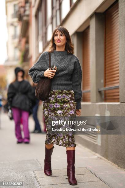 Jeanne Damas wears gold earrings, a dark gray braided wool pullover, a dark brown suede shoulder bag, a dark brown with purple and green flower print...