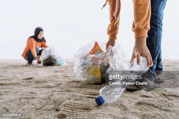 mother and daughter cleaning up a beach - muslim woman beach stock pictures, royalty-free photos & images