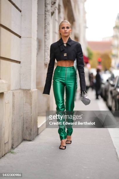Caroline Daur wears a black cropped jacket with silver metallic buttoned, high waist green shiny zipper waist cigarette pants, a silver sequined...