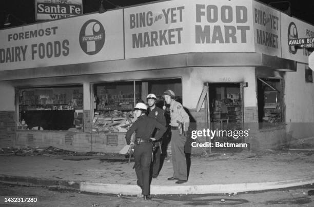 Police officers patrol a corner in the Watts district of Los Angeles, near a market which had its windows broken and door torn away by rioters.