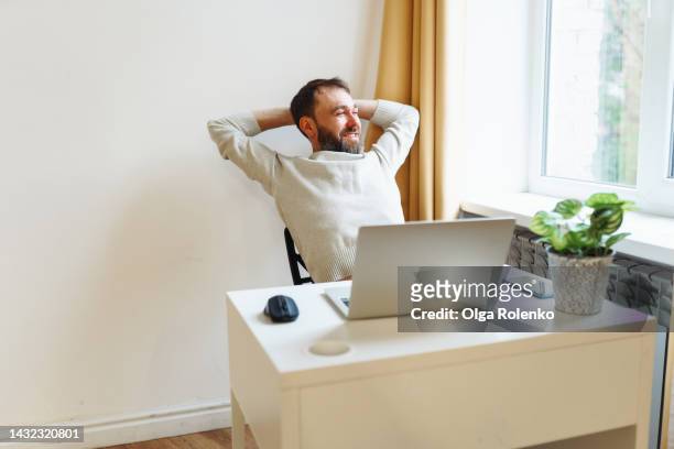 working at home office. relaxed man with hands behind his head looking out window in comfortable office - zurücklehnen stock-fotos und bilder