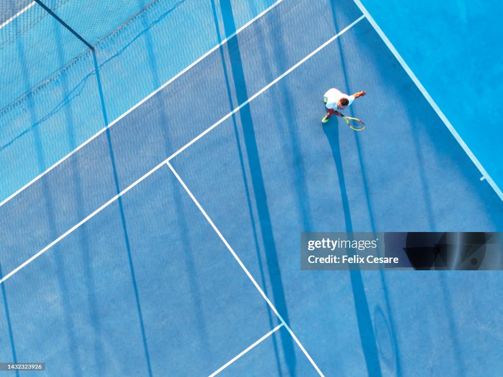 Aerial view of a young adult playing tennis on a blue hard court.