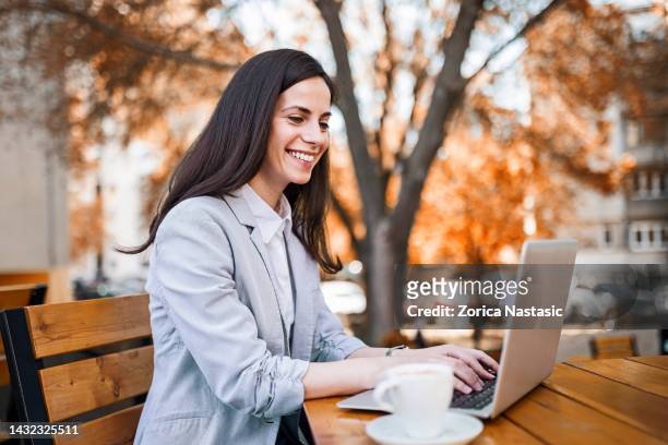 young businesswoman sitting in a sideway cafe, drinking coffee working on laptop - stirring stock pictures, royalty-free photos & images
