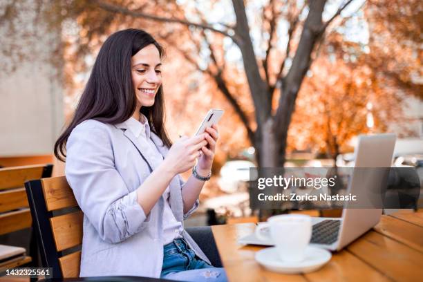 beber café usando una computadora portátil que sostiene un teléfono inteligente - combinación fotografías e imágenes de stock