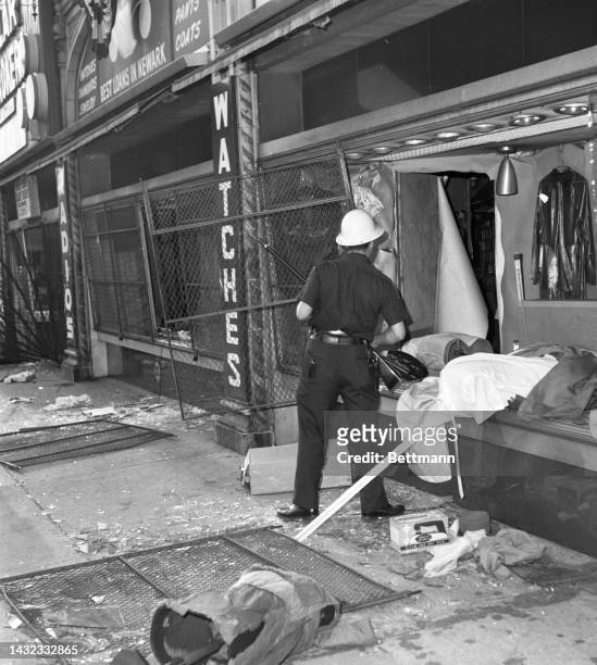 Helmeted police officer looks over the debris of a looted store window as New Jersey's largest city witnessed a second night of rioting.