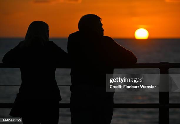 Couple watch as the sun sets viewed from Chesil Beach, on October 10, 2022 in Portland, England.