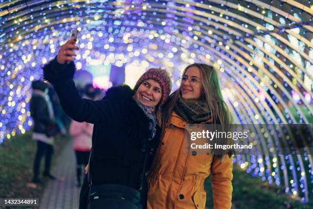 mother and daughter taking selfies in a tunnel with christmas lights in public park - christmas poland stock pictures, royalty-free photos & images