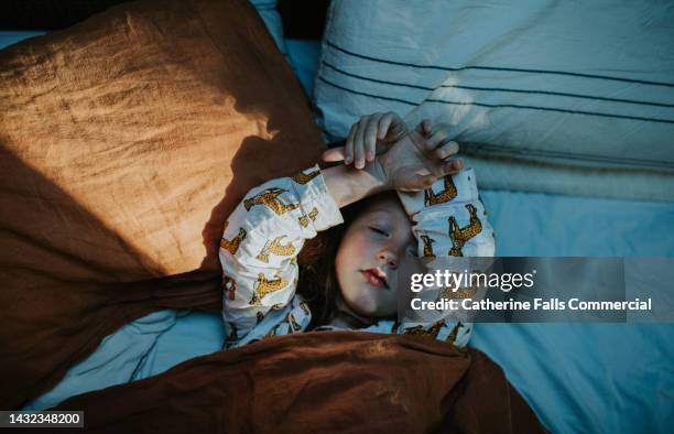 a little girl lies in bed, wrapped in a cozy duvet - hot night bed photos et images de collection