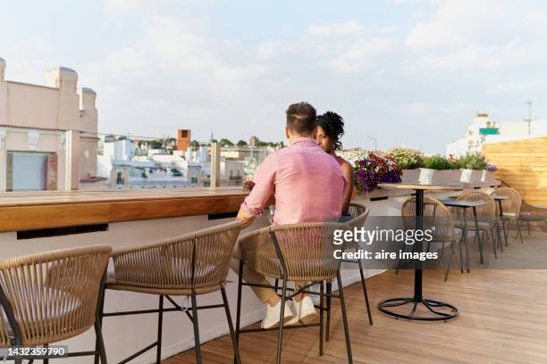 rear view of caucasian man seated conversing at the terrace bar in front of a beautiful young curly-haired black woman - terrasse bar stock-fotos und bilder
