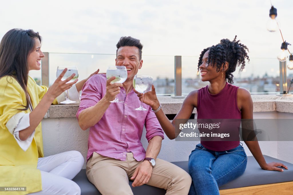A smiling white woman seated holding a cup next to her a man holding a cup and next to the man a colored woman holding a cup