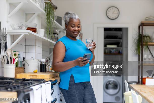 woman drinking water and checking her cell phone after her home workout - senior adult on phone stock pictures, royalty-free photos & images