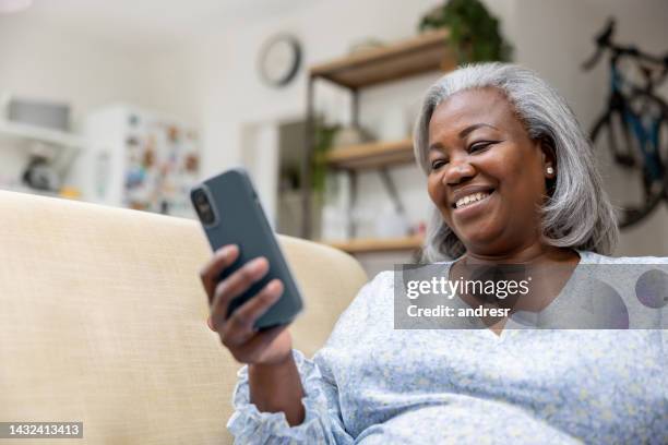 woman at home looking happy watching videos on her cell phone - middle aged woman at home stock pictures, royalty-free photos & images