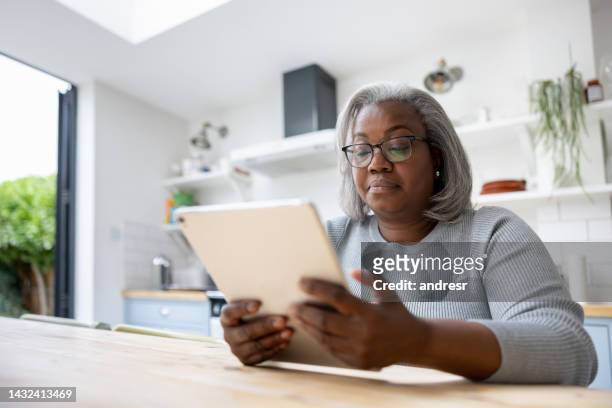 mature woman at home reading on her tablet - adult reading stock pictures, royalty-free photos & images