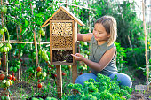 Portrait of happy girl next to hotel for insects in  of wooden birdhouse in garden