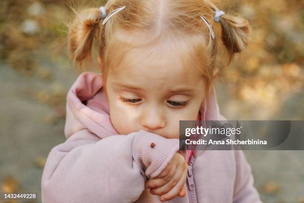 surprised little girl looking at a ladybug on her hand. white cute toddler with blue eyes. lovely blonde baby in a pink sweatshirt. autumn background. - coccinella stockfoto's en -beelden