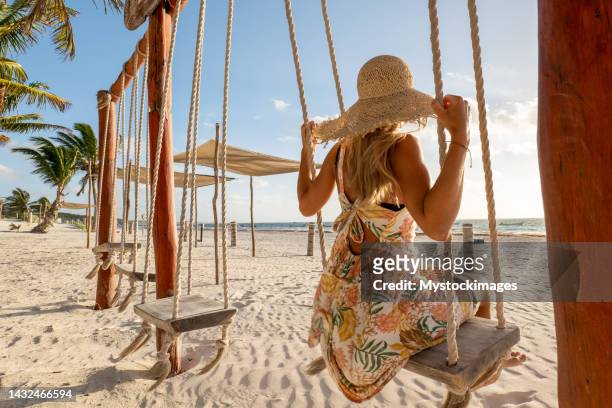 young woman having fun swinging on the beach at sunrise - tulum mexico 個照片及圖片檔