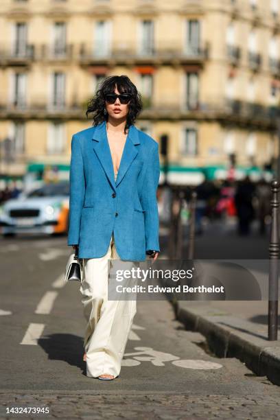 Xiayan wears black sunglasses, a blue wool long blazer jacket, silver earrings, a mint green lace bra underwear, a black and white shiny leather...