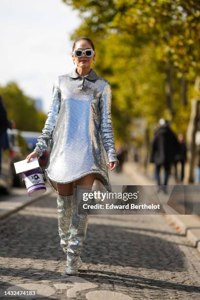 Araya Hargate wears white latte puffy square sunglasses from Loewe, silver earrings, a silver sequined long sleeves / short dress, a white and purple...