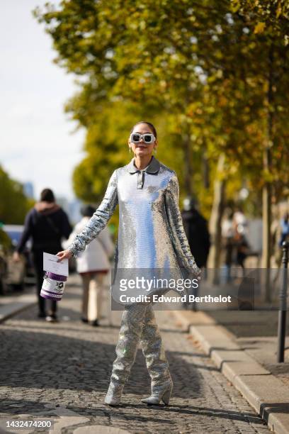 Araya Hargate wears white latte puffy square sunglasses from Loewe, silver earrings, a silver sequined long sleeves / short dress, a white and purple...