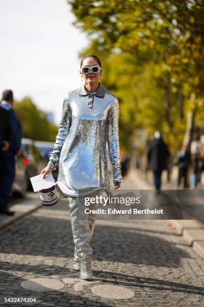 Araya Hargate wears white latte puffy square sunglasses from Loewe, silver earrings, a silver sequined long sleeves / short dress, a white and purple...