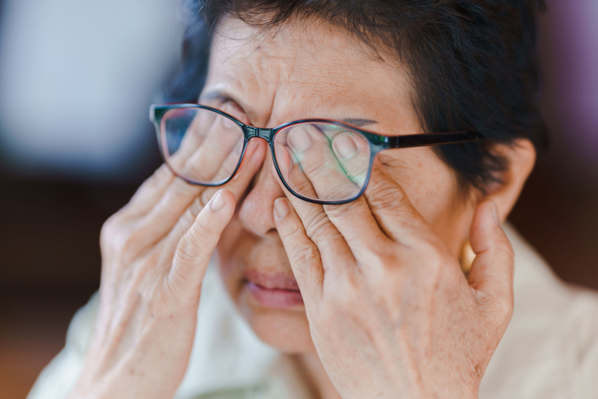 An elderly woman wears glasses and massages her eyes with her hands because of fatigue. Concept of health problems in the elderly. An elderly woman wears glasses and massages her eyes with her hands because of fatigue. Concept of health problems in the elderly.