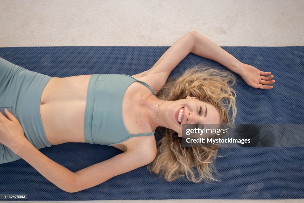 Portrait of sporty young woman resting on yoga mat, she smiles and laughs