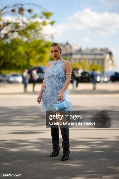 Justyna Czerniak wears black earrings, a pale blue feather halter-neck / sleeveless / short dress, a blue shiny metallic leather handbag, black shiny...