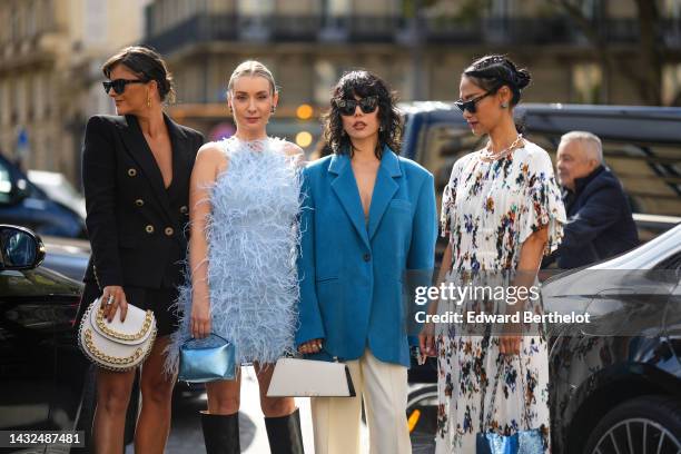 Gili Biegun wears black sunglasses, gold large logo earrings from Valentino, a black shoulder-pads / buttoned jacket, a matching black short skirt, a...