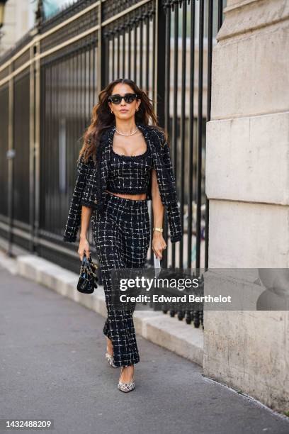 Hiba Abouk wears black sunglasses, silver and gold earrings, a diamonds necklace, a black and white checkered print pattern tweed cropped tank-top, a...