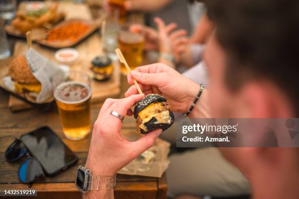 man holding a delicious black bun burger - little burger stock pictures, royalty-free photos & images