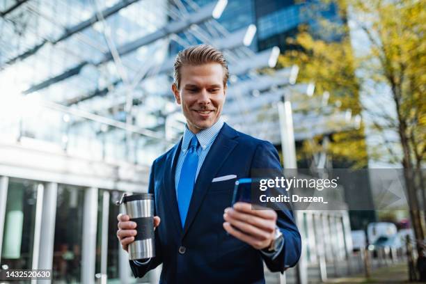 joven empresario con atuendo de negocios rojo y azul que usa el teléfono al aire libre para intercambiar criptomonedas - europeo del norte fotografías e imágenes de stock