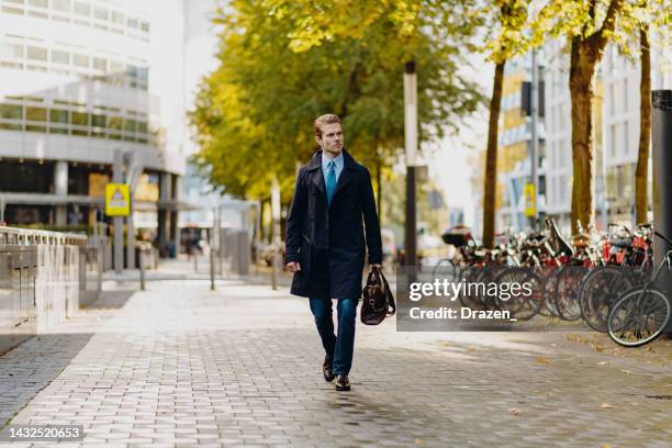 junger geschäftsmann geht mit ledertasche und blauem anzug zu arbeiten - ledertasche stock-fotos und bilder