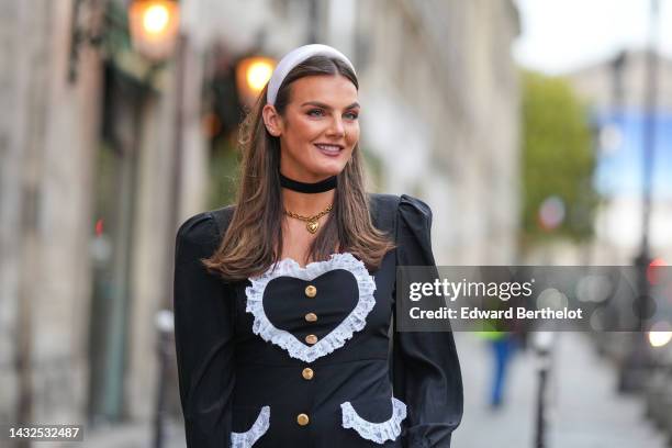 Guest wears a white large headband, gold earrings, a black large necklace, a gold large chain necklace, a black puffy long sleeves / gold buttons /...