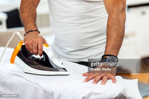 a  man at home ironing his button down shirt. - white button down shirt stock pictures, royalty-free photos & images