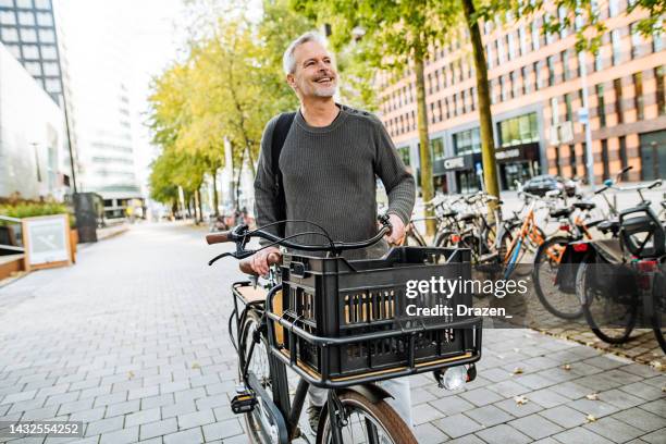 handsome mature man riding cargo bicycle and contributes to eco-friendly environment. businessman near green buildings - cycling netherlands stock pictures, royalty-free photos & images