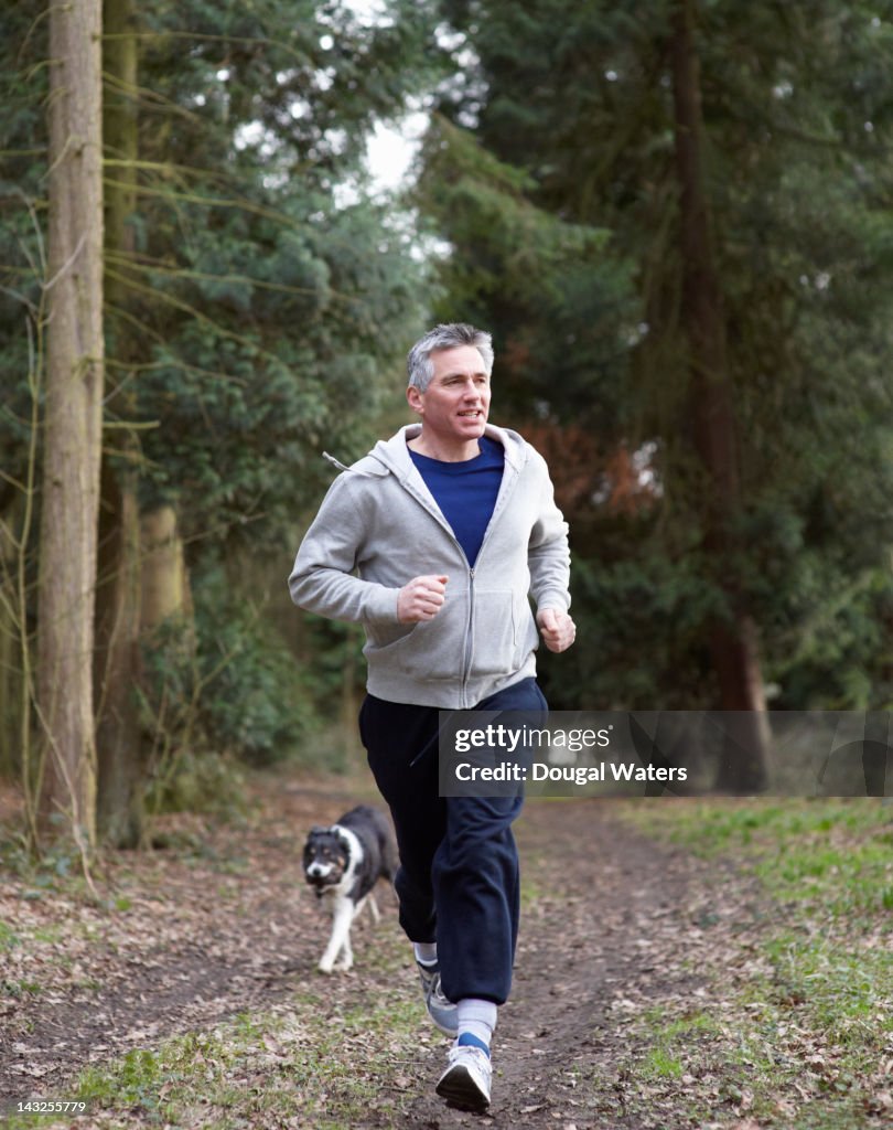 Man running in woodland with dog.