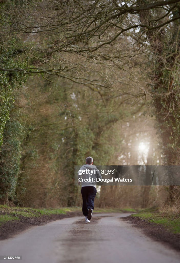 Man running toward sunburst on country lane.