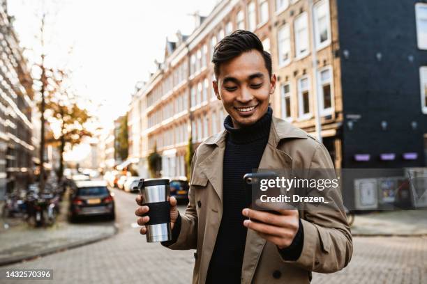 japanese man using smart phone for video call  and drinking coffee on the move - amsterdam business stock pictures, royalty-free photos & images