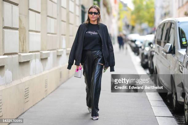 Guest wears black sunglasses from Off-White, silver earrings, a black with painted rhinestones t-shirt, a black nylon bomber coat, black shiny ripped...