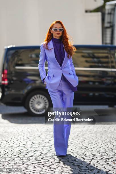 Guest wears gray plastic sunglasses from Prada, a dark purple turtleneck blouse, a purple blazer jacket, matching purple wide legs pants, dark purple...