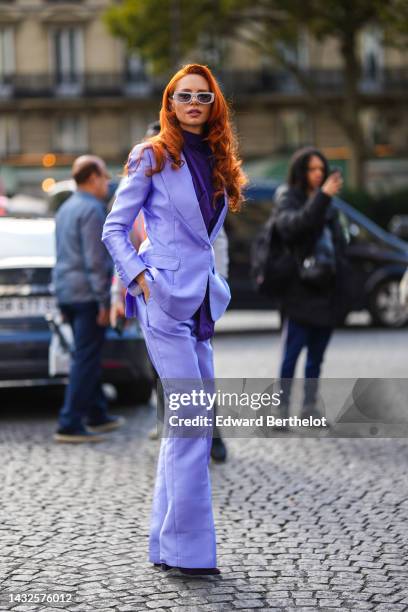 Guest wears gray plastic sunglasses from Prada, a dark purple turtleneck blouse, a purple blazer jacket, matching purple wide legs pants, dark purple...