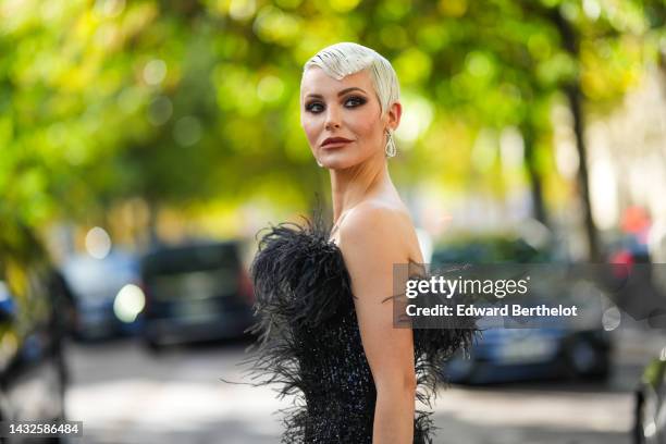 Guest wears silver and rhinestones earrings, a black feathers shoulder-bag / embroidered black to gold gradient sequined flared jumpsuit , outside...