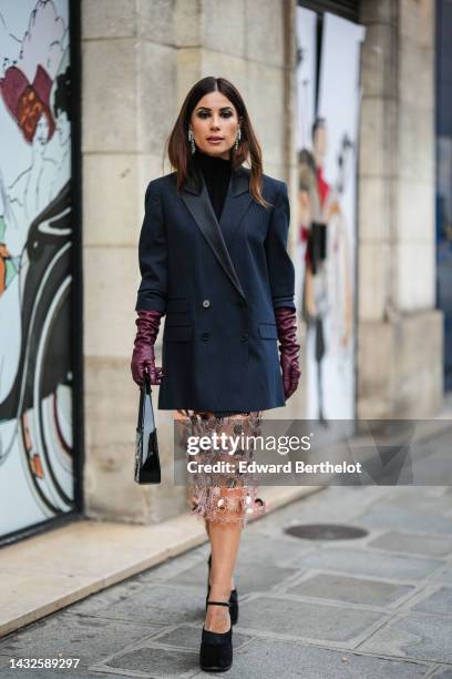 Guest wears silver and crystal fringed earrings, a black ribbed turtleneck pullover, a black striped print pattern blazer jacket, a burgundy shiny...